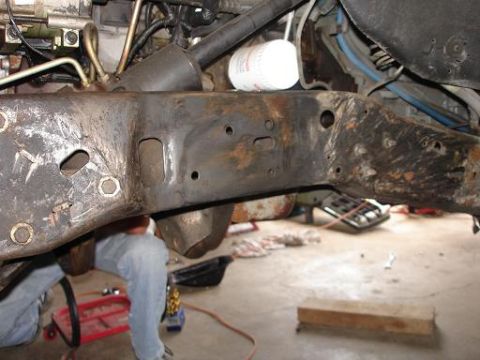 1996 Ford F-150 - A close-up view of a heavily rusted and worn truck frame, likely from a 1996 Ford F-150, with various bolts and holes visible. A person in…