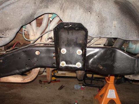 1996 Ford F-150 - The underside of a vehicle frame is shown, with a black metal bracket bolted to the frame with four large bolts. The exhaust manifold and p…