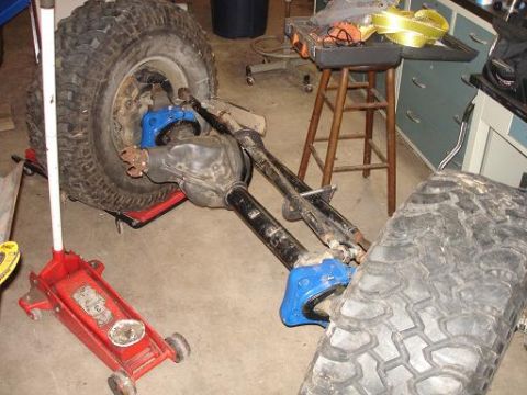 1996 Ford F-150 - A vehicle's rear axle assembly with a large tire is supported by a red hydraulic jack. Another tire lies in the foreground.