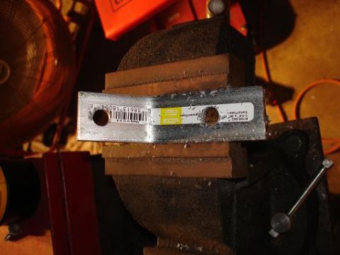 1996 Ford F-150 - A metal bracket with two holes is clamped in a vise. A barcode label is attached to the bracket.