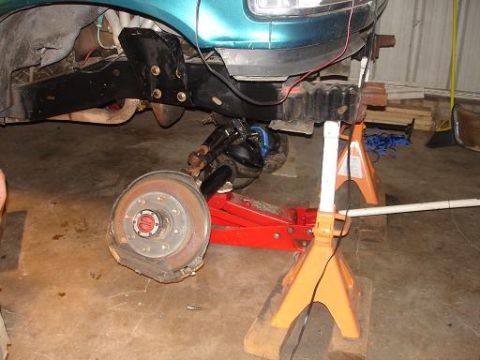 1996 Ford F-150 - A vehicle's front suspension and brake assembly are supported by a red hydraulic jack and orange jack stands in a garage setting. The vehic…