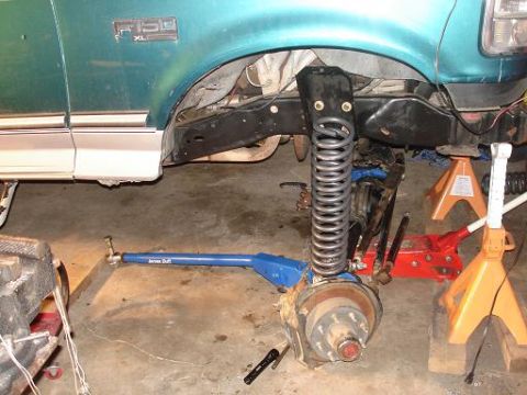 1996 Ford F-150 - The front suspension of a teal Ford F-150 pickup truck is shown disassembled, with the coil spring removed and resting on the ground. The v…