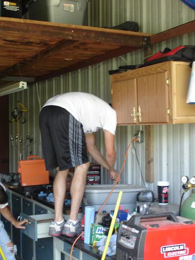 1996 Ford F-150 - A person in a white t-shirt and black shorts is bending over a workbench, plugging something into an electrical outlet. Various tools and e…