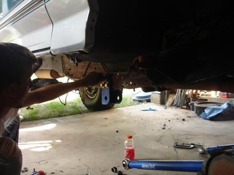1996 Ford F-150 - A person works on the underside of a pickup truck, with a blue suspension component and a bottle of drink visible on the ground.