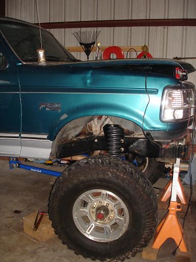 1996 Ford F-150 - The driver's side of a teal 1990s Ford F-150 pickup truck is shown in a garage setting. The vehicle is lifted with a large off-road tire an…