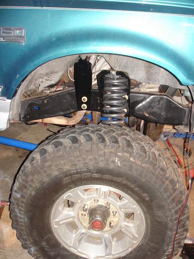 1996 Ford F-150 - A close-up view of the front suspension and tire of a teal Ford F-150 pickup truck, modified with a lifted suspension system. The image foc…