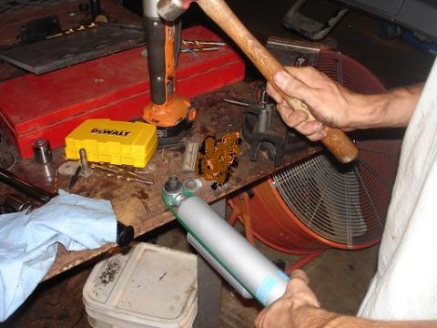 1996 Ford F-150 - A person is holding a hammer and a shock absorber over a workbench with various tools and a large fan in the background.