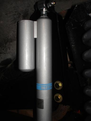 1996 Ford F-150 - A silver Bilstein remote reservoir shock absorber is mounted vertically. A blue stripe with white text is visible on the shock body.