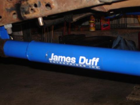 1996 Ford F-150 - A blue suspension component with white lettering that reads "James Duff Enterprises Inc." is mounted to a rusty vehicle frame.