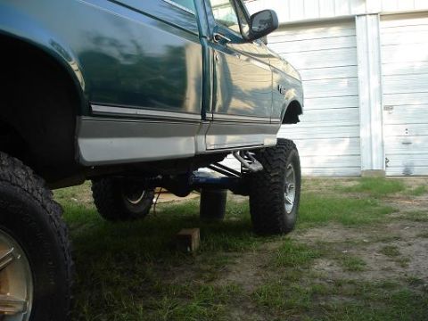 1996 Ford F-150 - The side view of a lifted, dark green pickup truck shows its large off-road tires and suspension components. The truck is parked on grass i…
