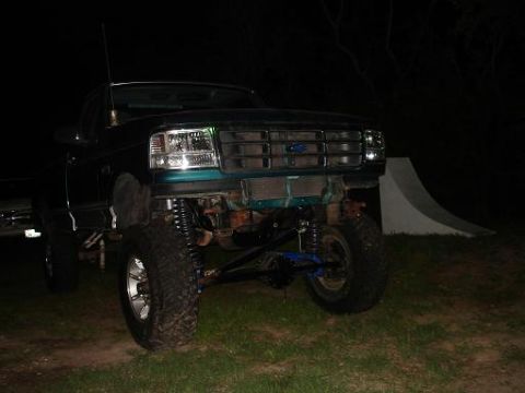 1996 Ford F-150 - A lifted, dark green Ford F-150 pickup truck is parked on grass at night. The front of the truck is visible, showing its headlights, grille…