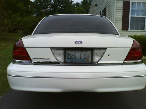 2003 Ford Crown Victoria - The rear view of a white 2003 Ford Crown Victoria LX is shown parked in front of a house. The license plate reads "225 FXW" and is from Mon…