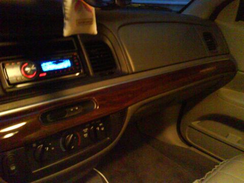 2003 Ford Crown Victoria - The interior of a car shows a car stereo with a blue display and a wood grain trim panel. A car air freshener hangs from the rearview mirro…