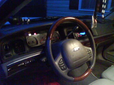 2003 Ford Crown Victoria - The interior of a car is shown, focusing on the steering wheel and dashboard. A digital display is visible on the dashboard.