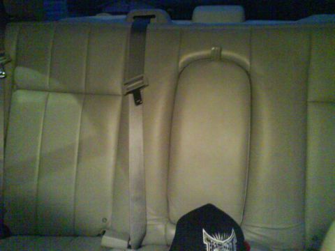 2003 Ford Crown Victoria - The interior of a car shows the back seat with a seatbelt and a black baseball cap on the seat. The seat is a light tan color and appears t…
