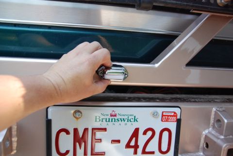 1996 Ford Bronco - Photograph of a hand operating a tailgate handle with a New Brunswick plate reading CME-420, not a technical document.