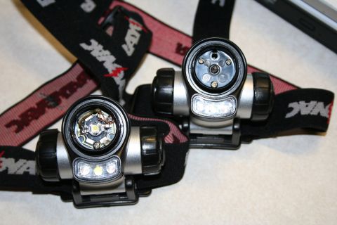 1984 Ford Bronco - Two Rayovac LED headlamps with black and red branded elastic straps laid on a light surface, both with the main reflector lens removed to e…