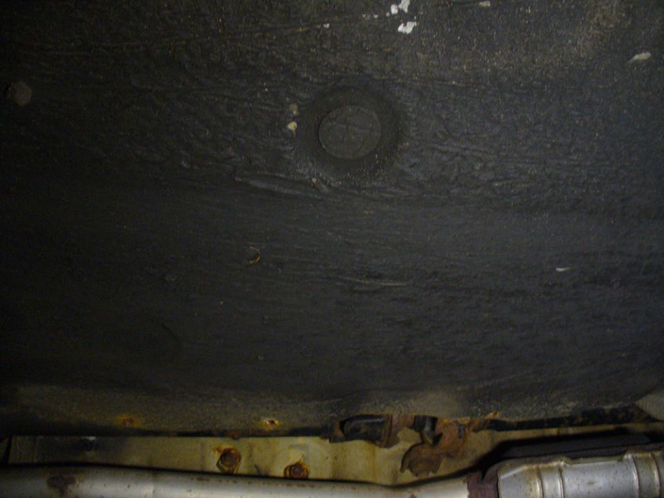 Underside of a vehicle showing undercoating, rust, and exhaust system.