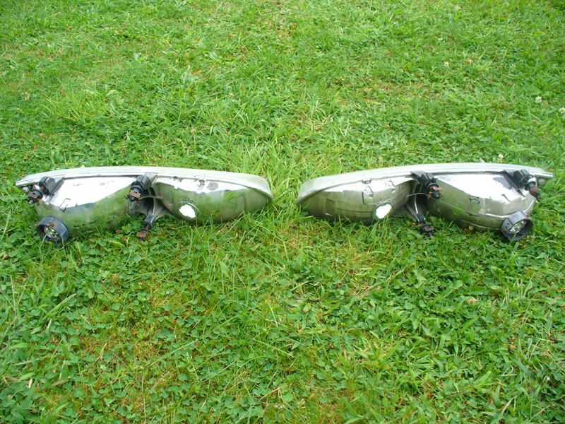 Rear side of two removed headlight assemblies on grass showing bulb sockets