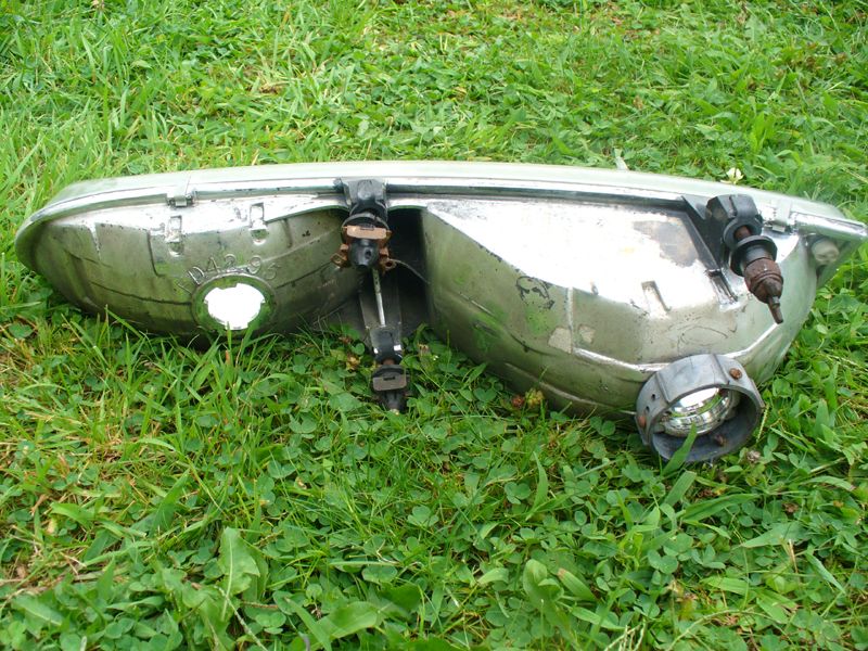 Back side of a used composite headlight assembly on grass with bulb sockets and adjusters