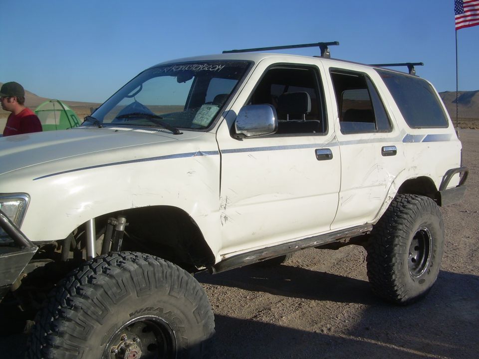 White lifted SUV with trail-scraped body panels parked at a desert camp