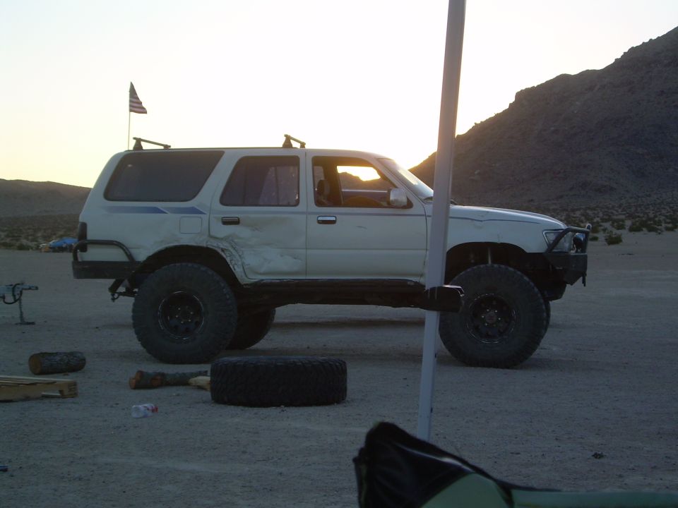 Side view of lifted white 4Runner at desert camp at dusk with body damage and mud tires