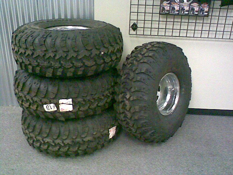 Set of four mud-terrain tires on polished aluminum wheels stacked indoors