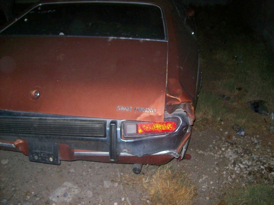 Damaged brown 1970s Ford Gran Torino rear passenger side at night.