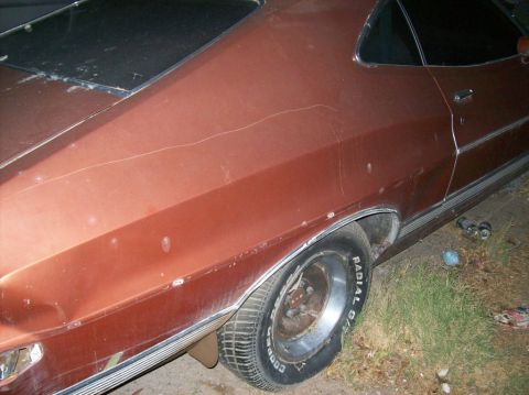 1975 Ford Ranchero - The rear quarter panel and wheel of a rusty, copper-colored classic car are shown in this close-up side view. The car has a black vinyl top…