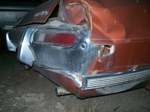 1975 Ford Ranchero - The rear of a heavily damaged, rusty orange car is shown. The taillight is intact but the surrounding bodywork and bumper are severely bent…