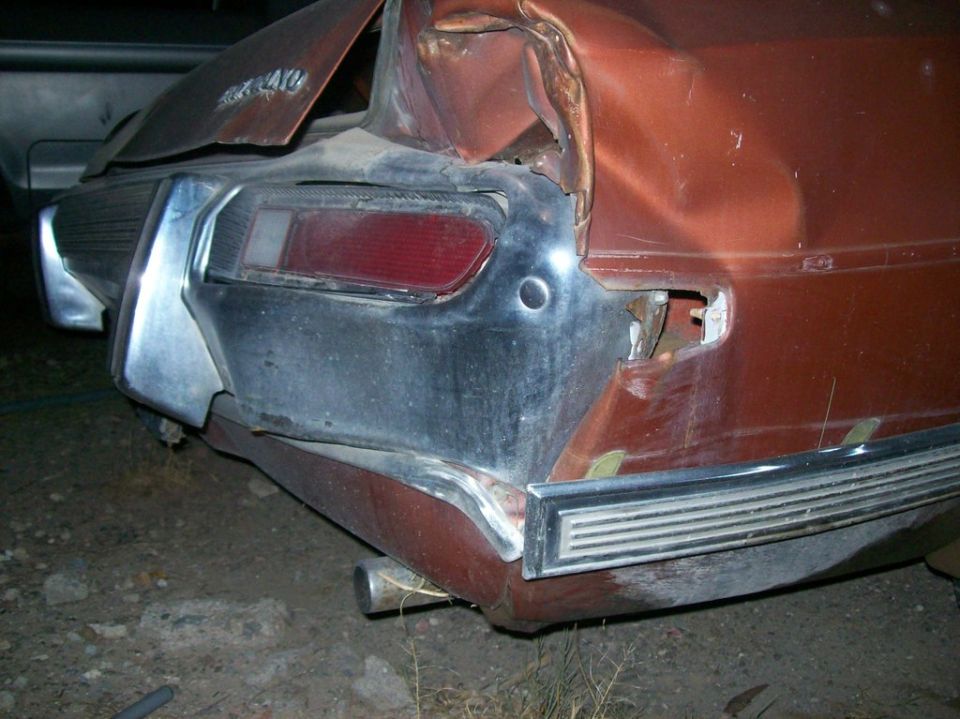 Heavily damaged rear of a rusty orange car, showing bent bodywork and bumper.
