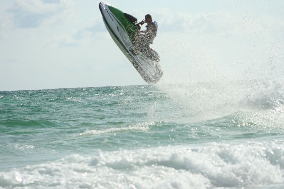 Green and white jet ski airborne over ocean waves with rider, spraying water under a hazy sky.