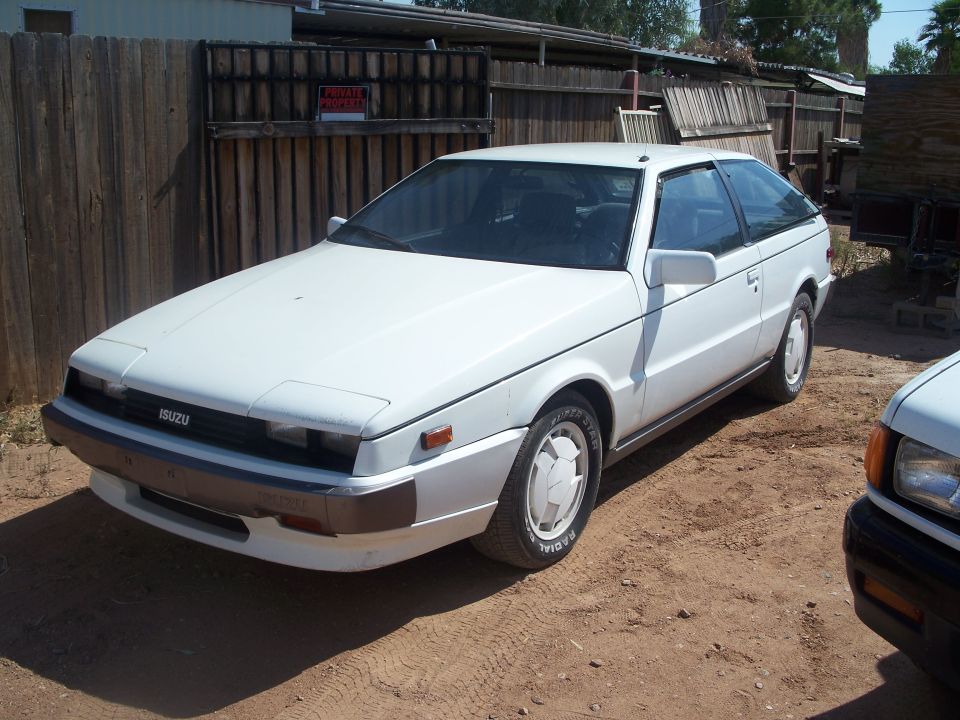 Side front view of a white Isuzu hatchback coupe on dirt