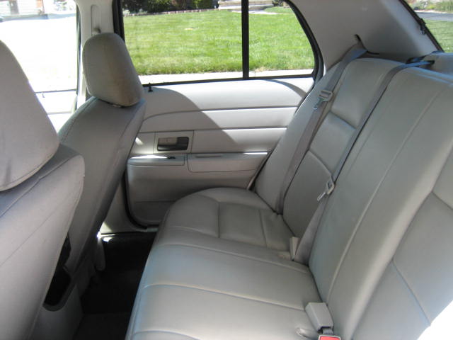 Rear interior of a light-colored sedan, showing leather seats and seat belts.