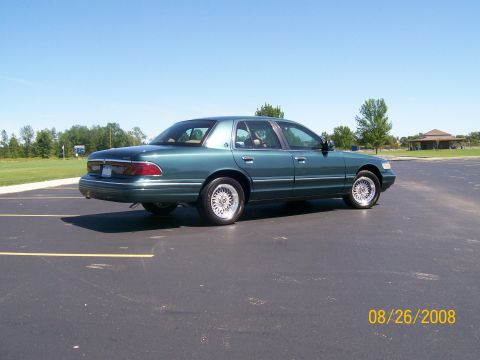 1995 Mercury Grand Marquis - A dark green sedan is parked in an empty asphalt lot on a sunny day. The car is viewed from the rear quarter angle, showing its side profil…