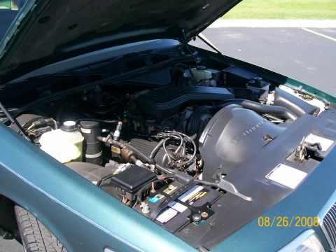 1995 Mercury Grand Marquis - The open hood of a dark teal sedan reveals its engine bay, including the battery, various fluid reservoirs, and engine components. A date s…