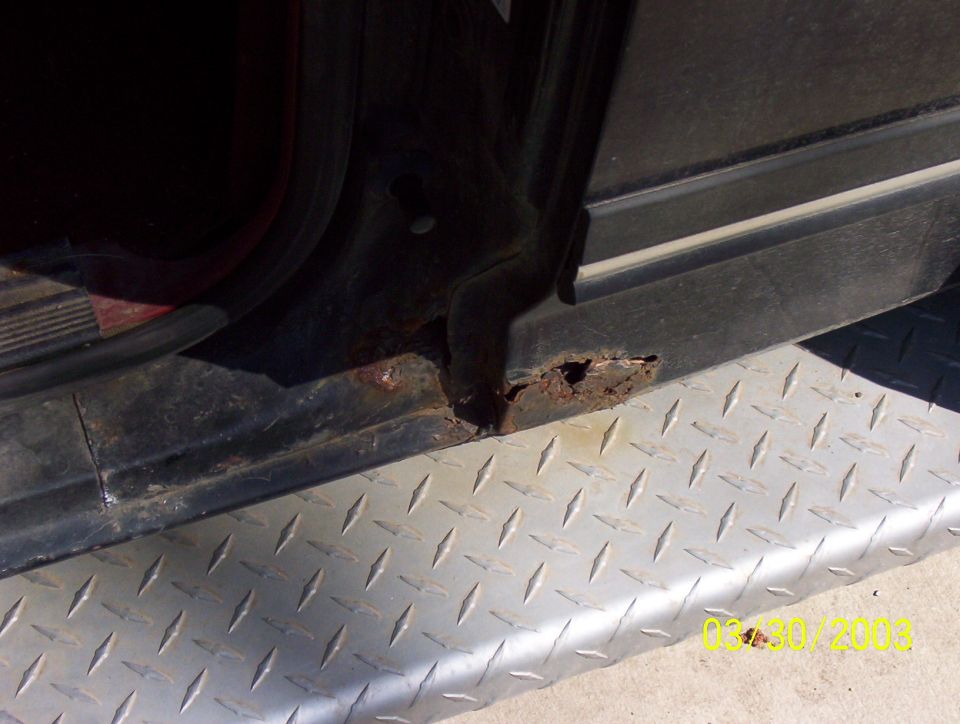 Rust holes through black truck rocker panel above aluminum diamond-plate running board