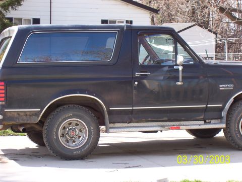1987 Ford Bronco - Side profile of a black 1987 Ford Bronco with chrome trim and aftermarket wheels.