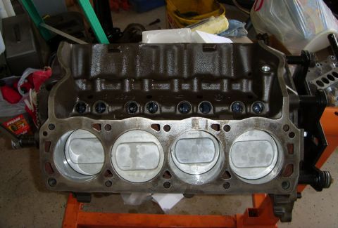 1989 Ford F-250 - A close-up, straight-on view of a V8 engine block with pistons installed. The engine block is dark brown and appears to be in a workshop or…