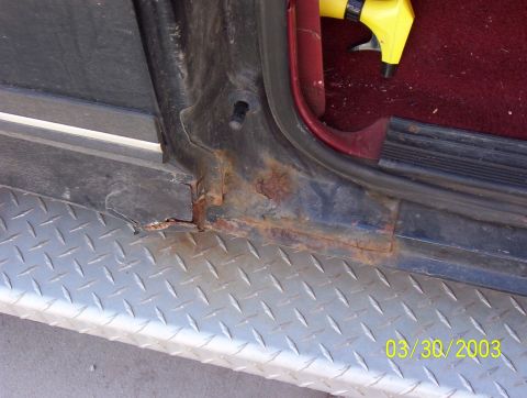 1987 Ford Bronco - The door frame of a vehicle shows significant rust damage, with diamond plate trim visible below.