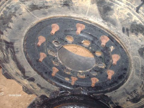 1990 Ford F-150 - A close-up view of a large, dirty tire and wheel assembly with multiple rusty lug bolts. The tire has text indicating its size and type.