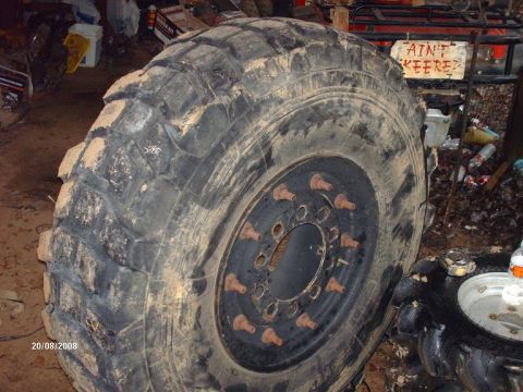 1990 Ford F-150 - A very large, muddy tractor tire with visible lug nuts is the main focus of the image. In the background, there is a red ATV with a sign th…