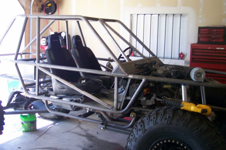 Custom tube chassis buggy with racing seats and exposed engine in a garage.