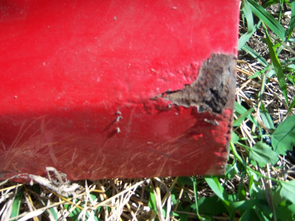 Close up of rusted edge on red vehicle part with grass.