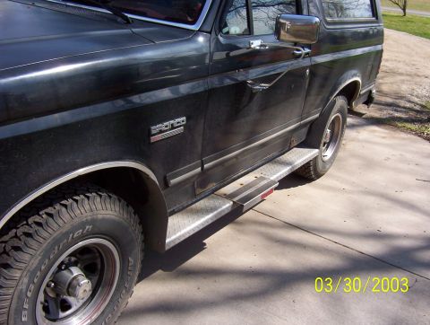 1987 Ford Bronco - Side view of a black 1987 Ford Bronco, showing its running boards and the 'Bronco' badge on the fender.