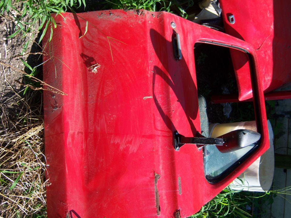Red vehicle door with black side mirror and handle on the ground.