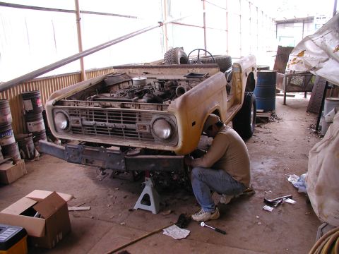 1971 Ford Bronco - A man works on the front end of a yellow Ford Bronco in a garage.