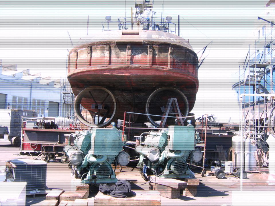 Large red vessel with propellers, industrial engines, and equipment in a shipyard.