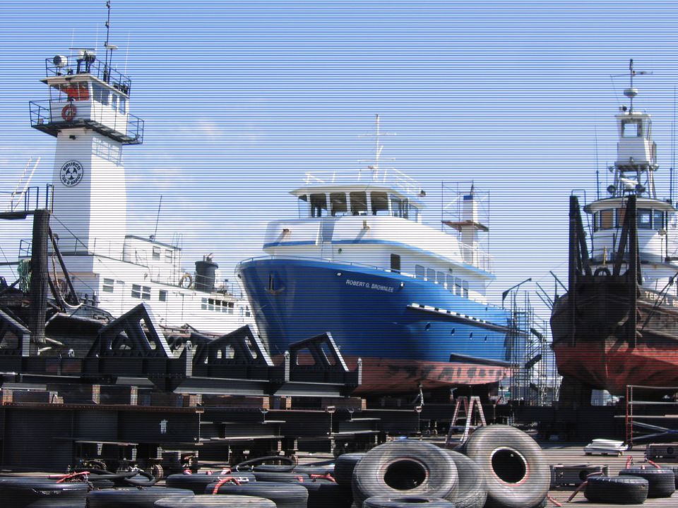Blue and white ship "ROBERT G. BROWNLEE" in shipyard with tires in foreground