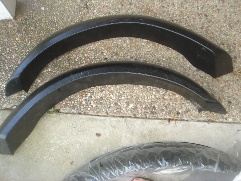 Two black fender flares on concrete, with a third in plastic wrap.